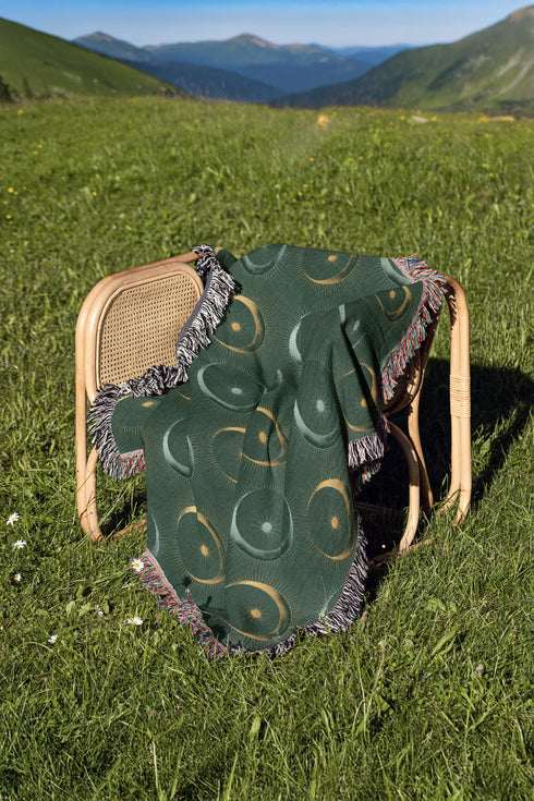 Forest green cotton throw blanket with woven silver moon phases and golden sun motifs, finished with multicolored fringe trim.